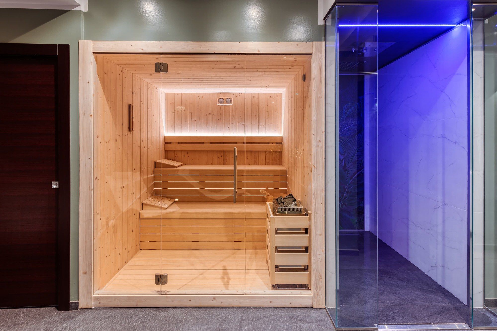 La sauna vista dalla sala, con la porta a vetri e la luce blu