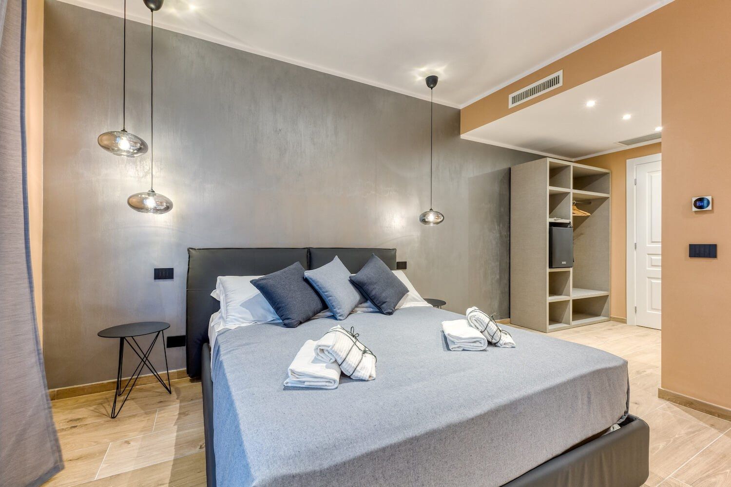 Pasifae: il letto con le lampade a sospensione e il grigio materico della parete